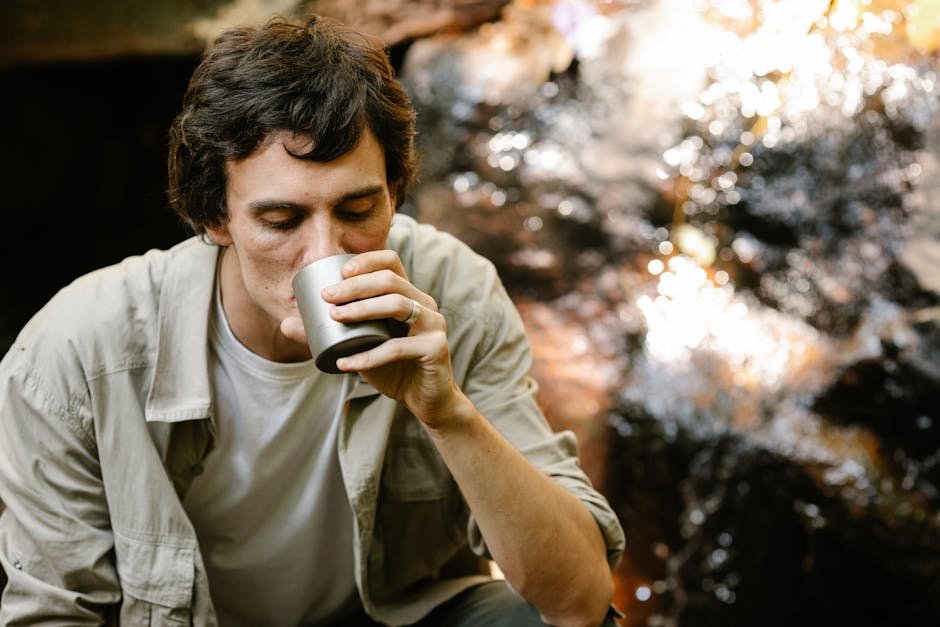 Calm male relaxing and having cup of tea on blurred background of clean stream